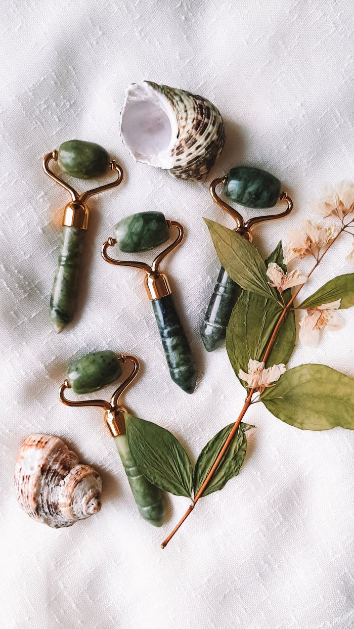 Elegant jade rollers alongside seashells and leaves on a fabric background for a serene beauty ritual.